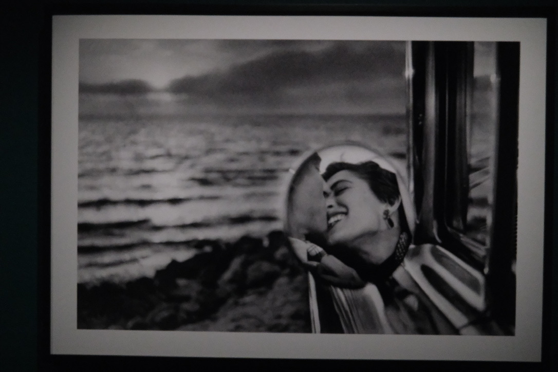 Black and white—couple kissing, reflected in a car side mirror by the sea at sunset