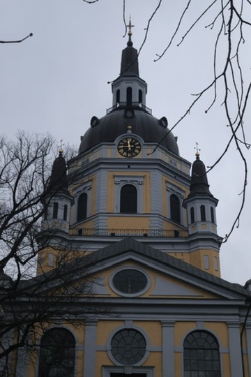 Church dome and clock tower against a winter sky, bare branches in the foreground