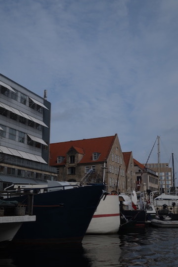 Boats in a European harbor, gabled buildings and masts under a soft overcast sky